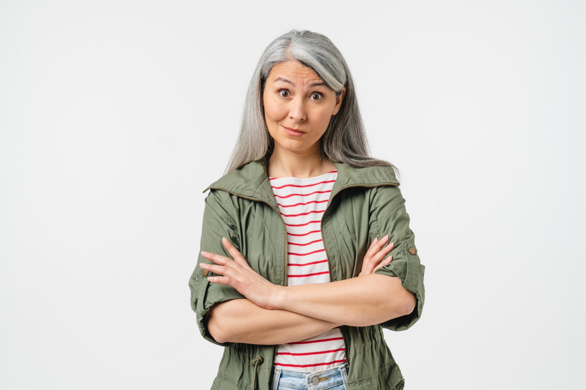 Exasperated Caucasian middle-aged woman in casual clothes is pursing her lips with arms crossed against a plain white background.